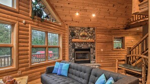 A log cabin interior with a stone fireplace, a sofa with blue cushions, and a wooden staircase. - 'camp Tony' w/ Trail Access: Walk to Lake Huron! (Millersburg)