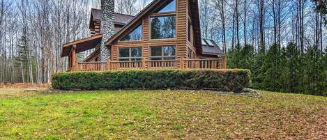 A log cabin with a stone chimney, large windows, and a well-maintained lawn.