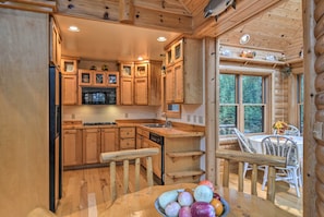 Cocina de cabaña de madera con comedor, armarios de madera, un refrigerador y una mesa con un bol de fruta.