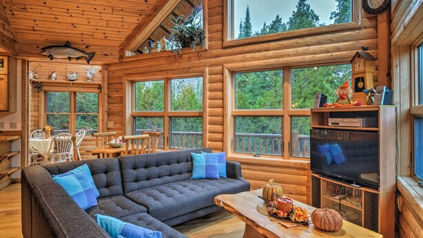 A cozy log cabin interior with a sectional sofa, wooden dining table, and a television. - 'camp Tony' w/ Trail Access: Walk to Lake Huron! (Millersburg)