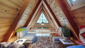 A cozy attic bedroom with a sloped ceiling, a window, a sofa, a small table, and a lamp. - Decks, Grills + Fire Pit: Camp Connell Hideaway! (Arnold)