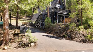 A cabin with a wooden deck and stairs leading to a loft bedroom, surrounded by trees and a dirt path. - Decks, Grills + Fire Pit: Camp Connell Hideaway! (Arnold)