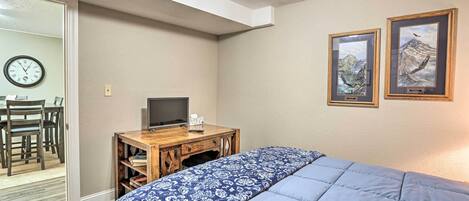 Een slaapkamer met een bed, een bureau met een computer, een klok en twee ingelijste foto’s aan de muur.