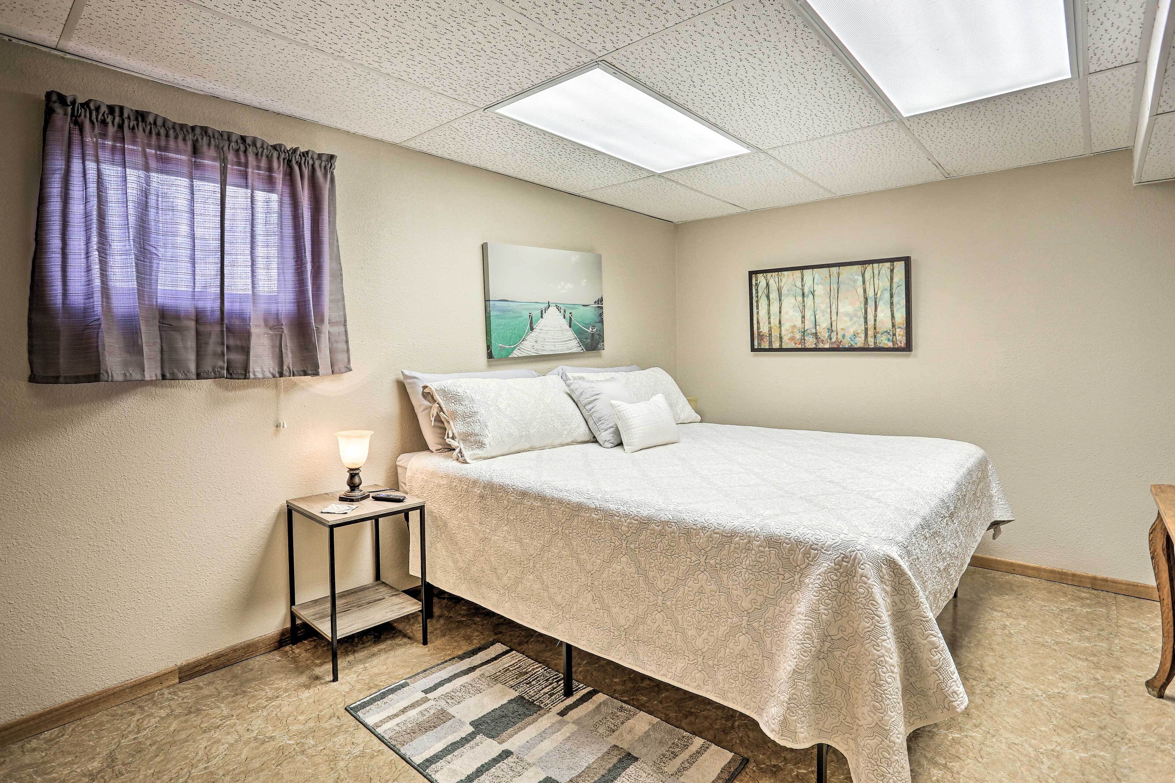 A bedroom with a bed, a nightstand, a lamp, a window with curtains, and two wall-mounted pictures.