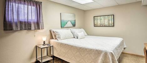 A bedroom with a bed, a nightstand, a lamp, a window with curtains, and two wall-mounted pictures.