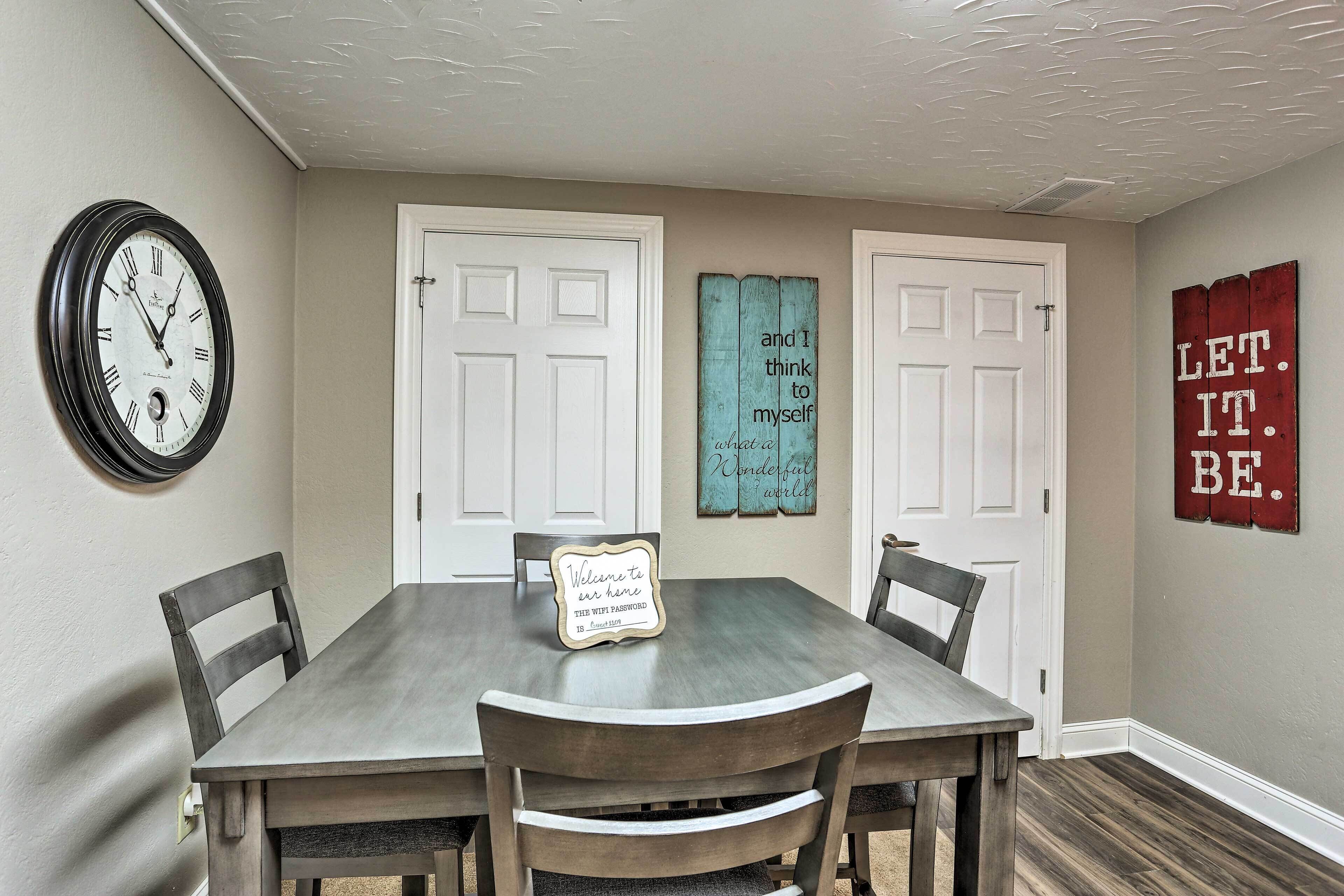 A dining area with a wooden table, four chairs, a wall clock, and decorative signs on the doors.