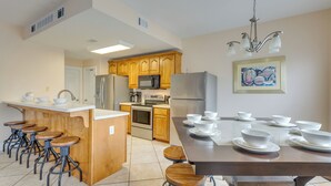 A modern kitchen with wooden cabinets, stainless steel appliances, and a dining area with a large table and multiple stools. - 1 Mi to Beach Access: Spacious Orange Beach Duplex (Orange Beach)
