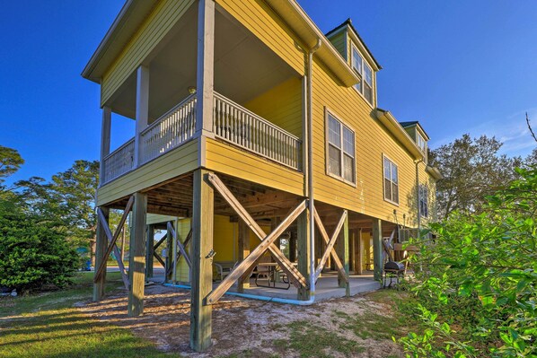 A two-story yellow house with a balcony, wooden support beams, and a picnic table in the yard.