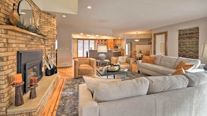 A spacious living room with a fireplace, comfortable seating, and a kitchen in the background. - Charming Joliet Ranch House on a Working Farm (Joliet)