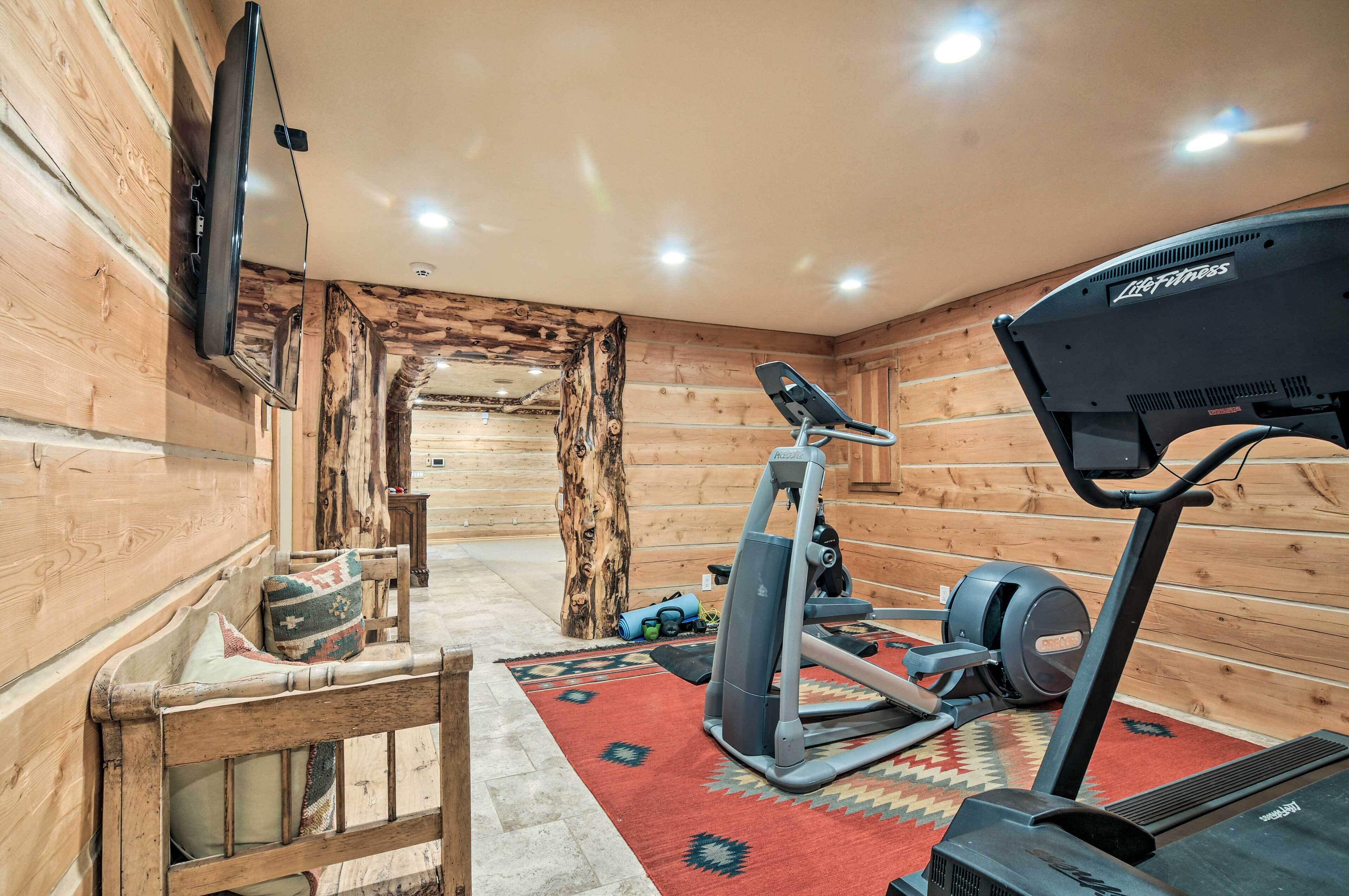 A log cabin with a treadmill, exercise equipment, a TV mounted on the wall, and a wooden bench.