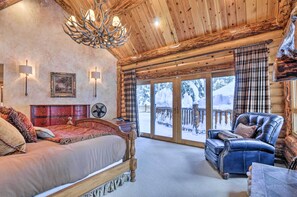 Ein Holzhütten-Interieur mit einem Bett, einem Ledersessel und einem großen Fenster mit Blick auf eine verschneite Landschaft.