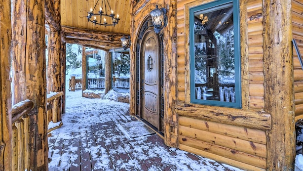 A log cabin with a wooden exterior, a snow-covered deck, and a large window.