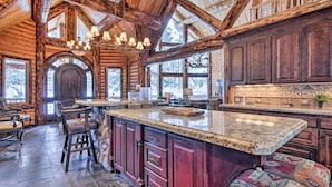 A spacious log cabin interior with a large kitchen island, stone countertops, and a high ceiling with exposed beams.