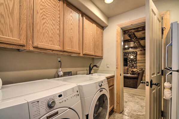 A laundry area with a washing machine and dryer, wooden cabinets, a sink, and a stone wall in the background. - Delightful Duck Creek Village Cabin w/ Deck! (Duck Creek Village)