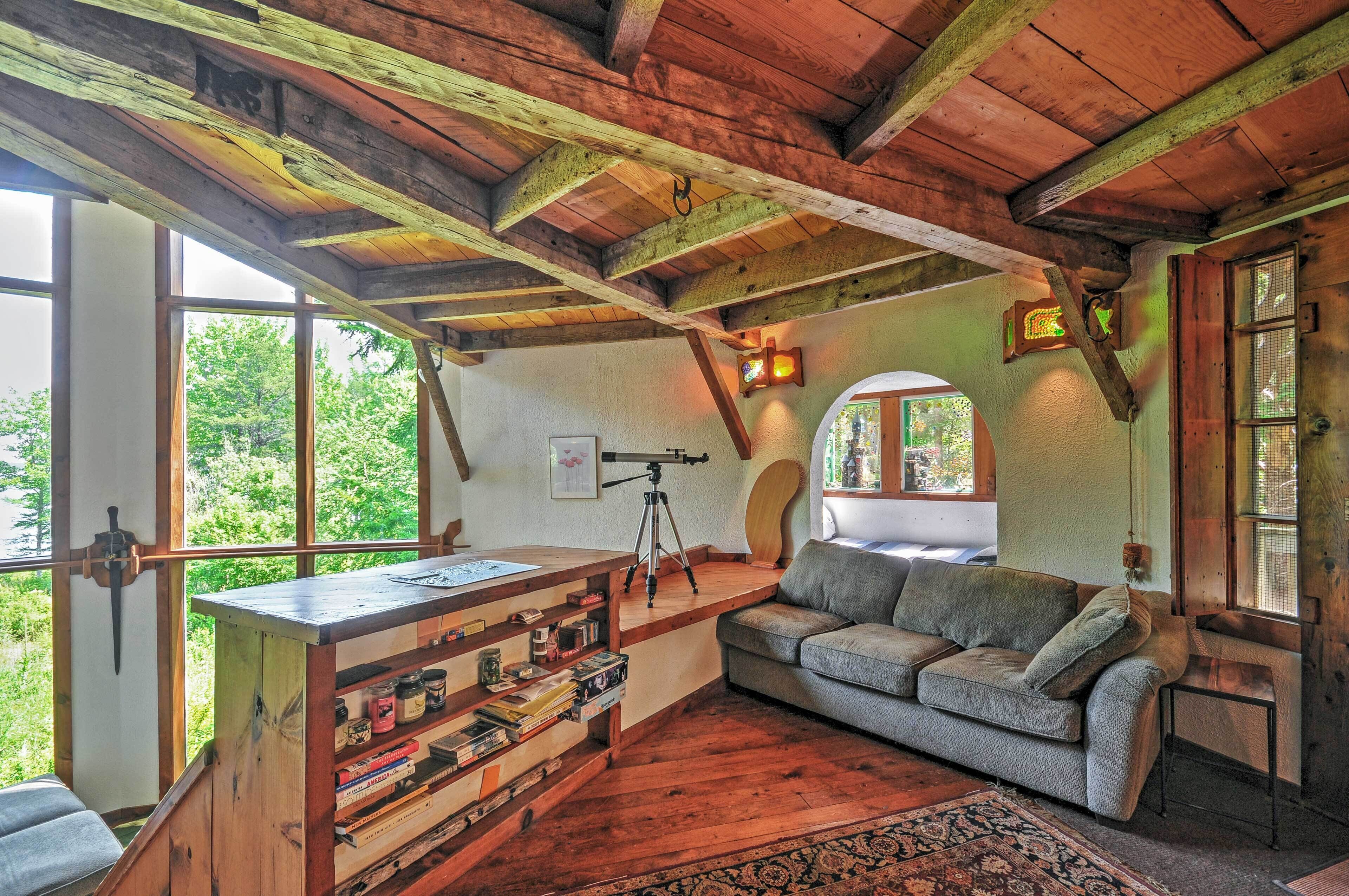 Een landelijk houten interieur met een houten plafond, een telescoop op een bureau, een bank en een boekenplank.