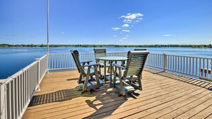 Eine Holzterrasse mit Metallgeländern, einem Tisch und zwei Stühlen mit Blick auf ruhiges Wasser.