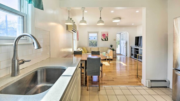 A modern kitchen with a large sink, dining area with a table and chairs, and a living room with a sofa and TV.