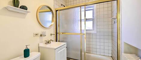Ein Badezimmer mit Toilette, Waschbecken, Spiegel, Duschkabine und gefliesten Wänden.