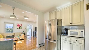 A modern kitchen with stainless steel appliances, a dining area with a wooden table and chairs, and cream-colored cabinetry.