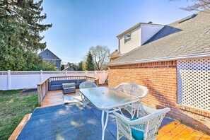 A backyard patio with a glass table and wicker chairs, a wooden deck, and a brick wall.