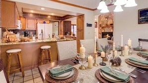 Una cocina luminosa con armarios de madera, un comedor listo para una comida con velas, y una chimenea al fondo.