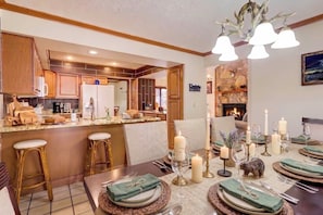 A well-lit kitchen with wooden cabinets, a dining area set for a meal with candles, and a fireplace in the background. - Hot Tub + Fire Pit: Creekside Gatlinburg Getaway! (Gatlinburg)