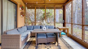 Un patio techado con un sofá de mimbre, una mesa de madera y vistas a árboles.
