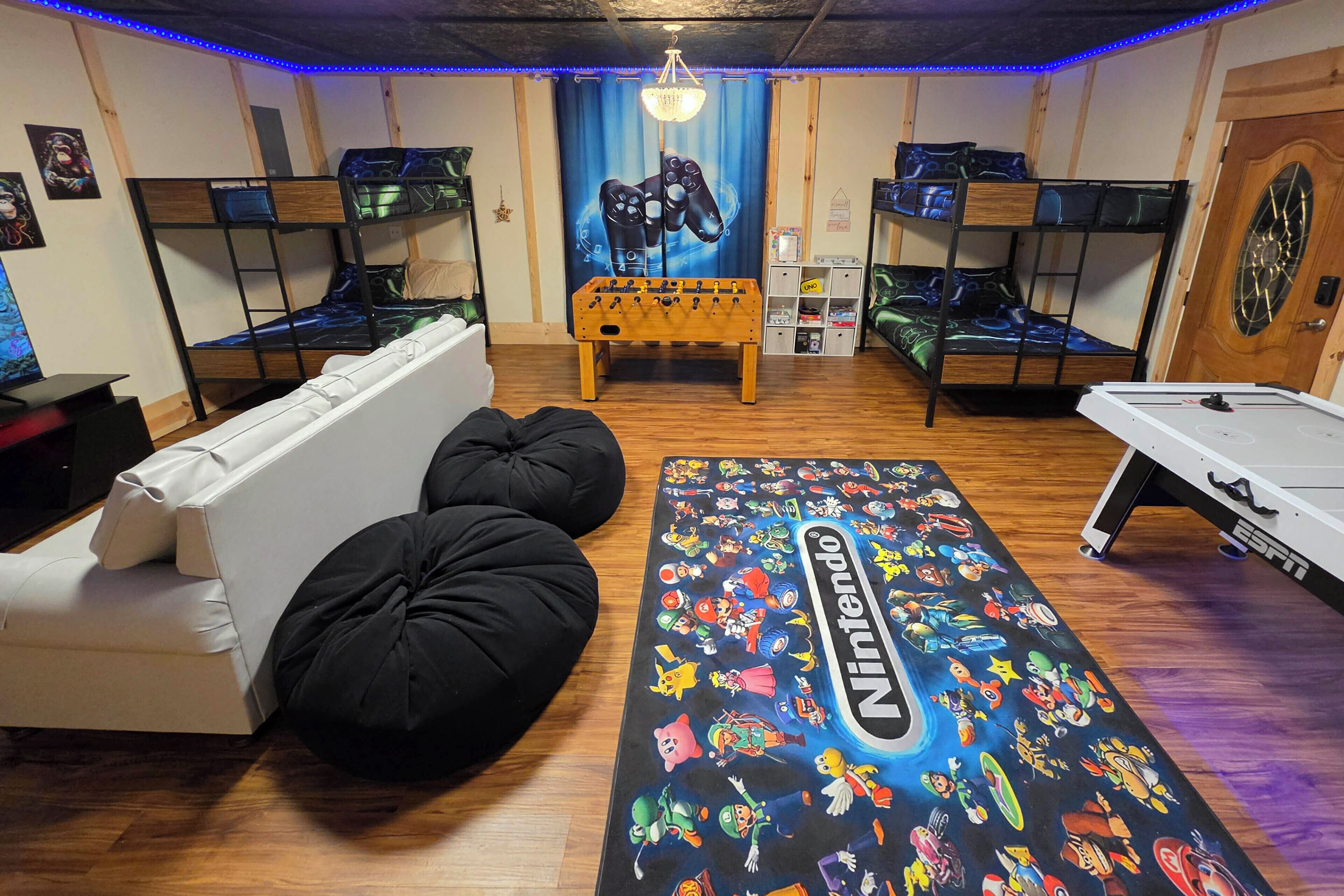 A room with bunk beds, a foosball table, a Nintendo-themed mat, and a pool table.