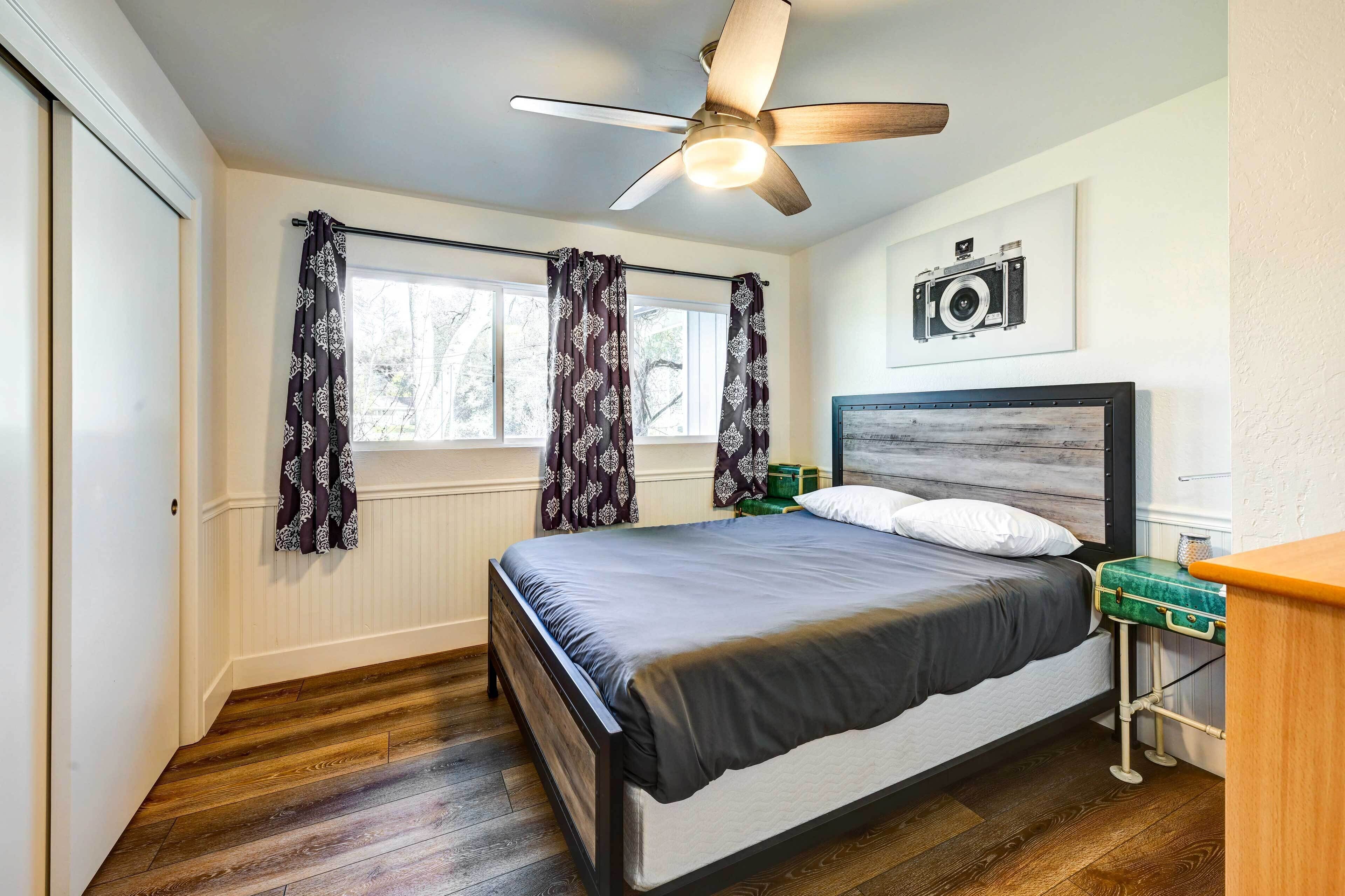 Une chambre à coucher comprenant un lit, un ventilateur de plafond, une fenêtre avec des rideaux, une caméra fixée au mur et une table de chevet.