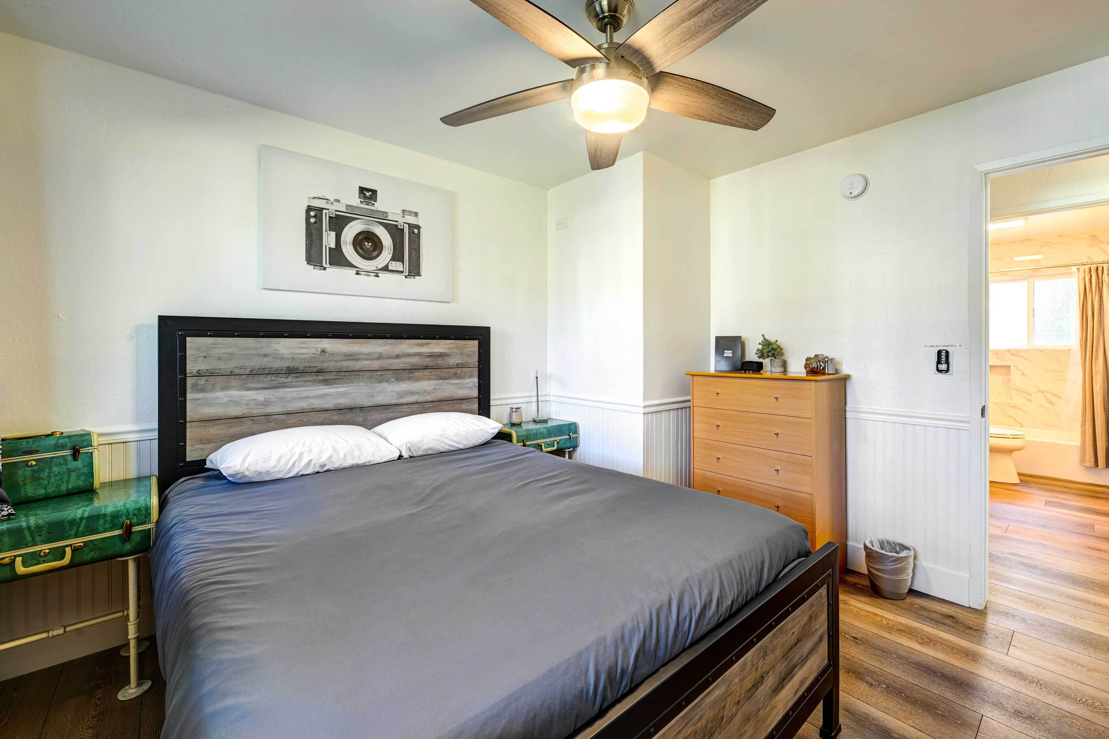 Een slaapkamer met een bed, een dressoir, een plafondventilator en een ingelijste foto aan de muur.