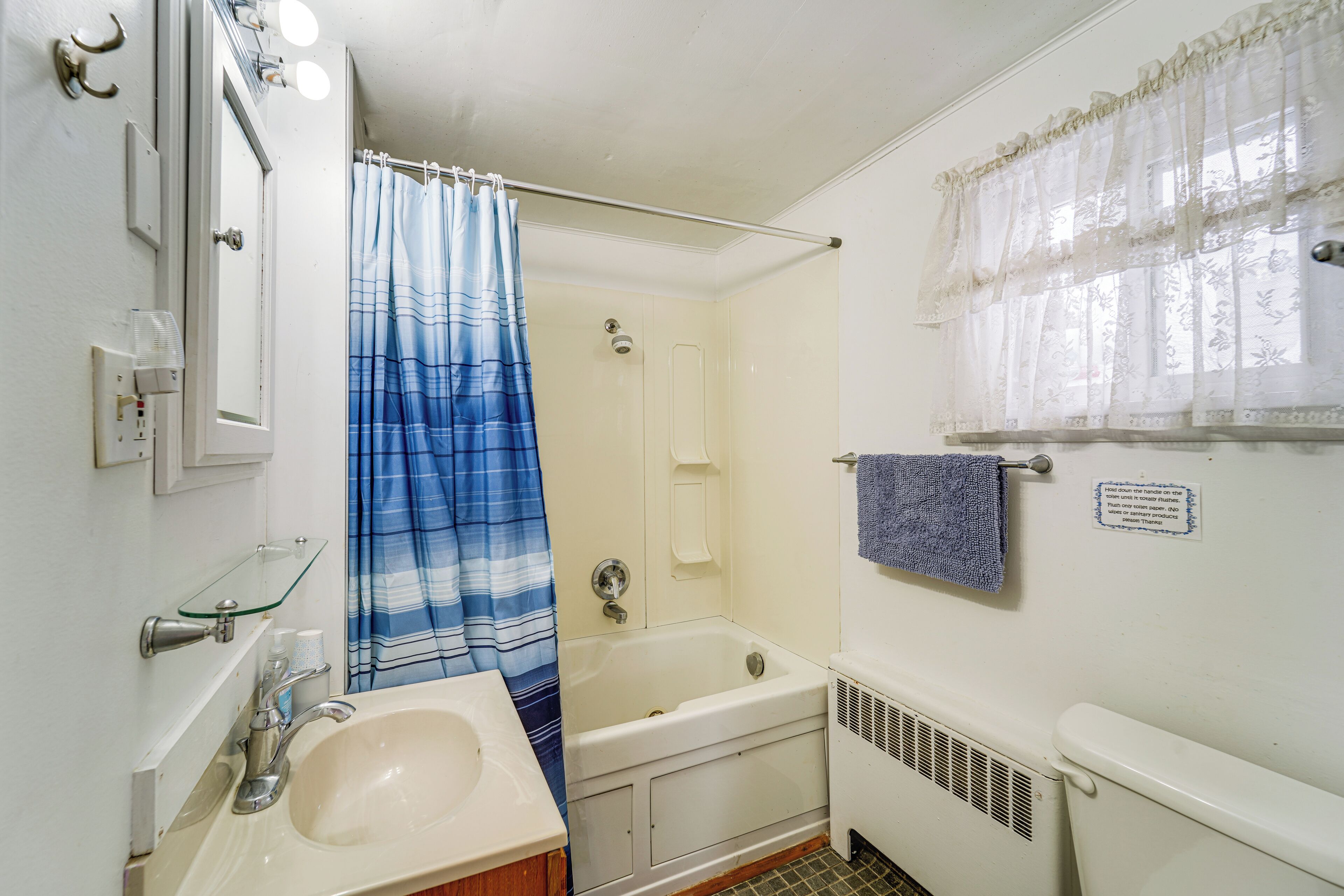 A bathroom with a bathtub, a sink, a glass shelf, a shower curtain, and a towel rack.
