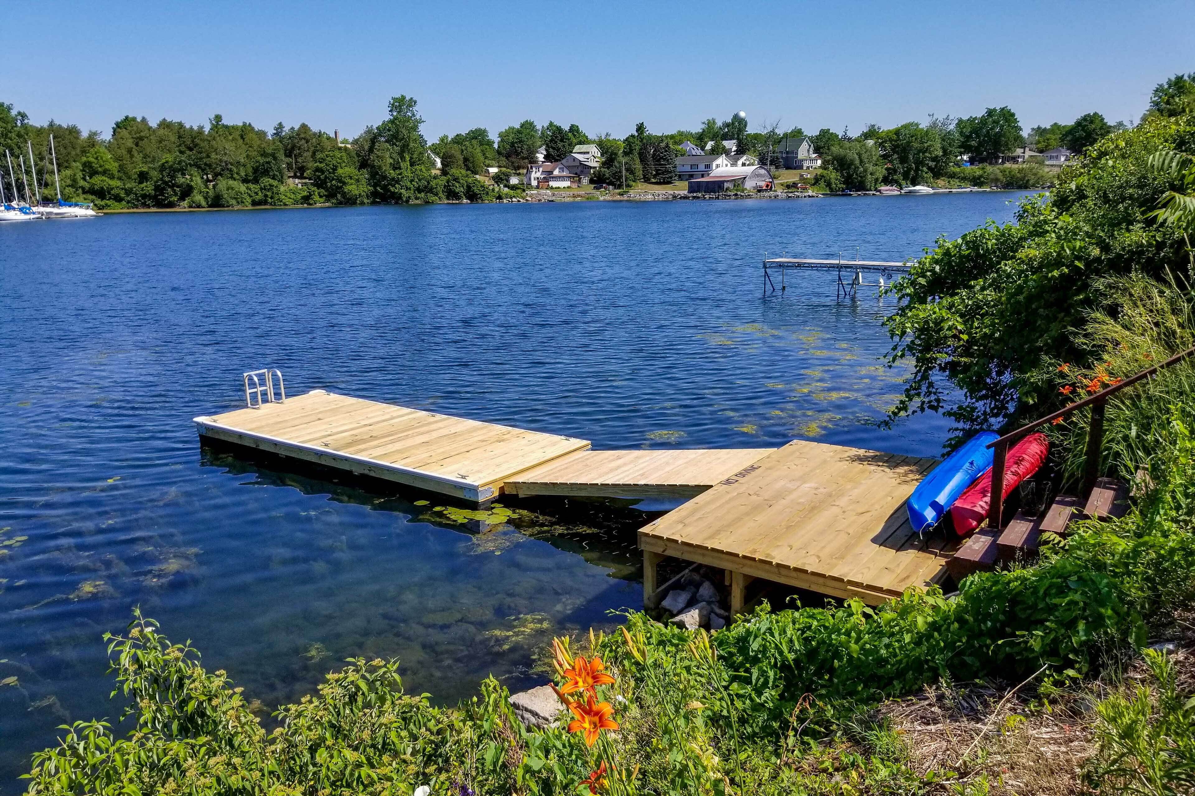 Eine Holzstege führt in einen ruhigen See mit klarem Wasser, umgeben von üppigem Grün und Häusern im Hintergrund.