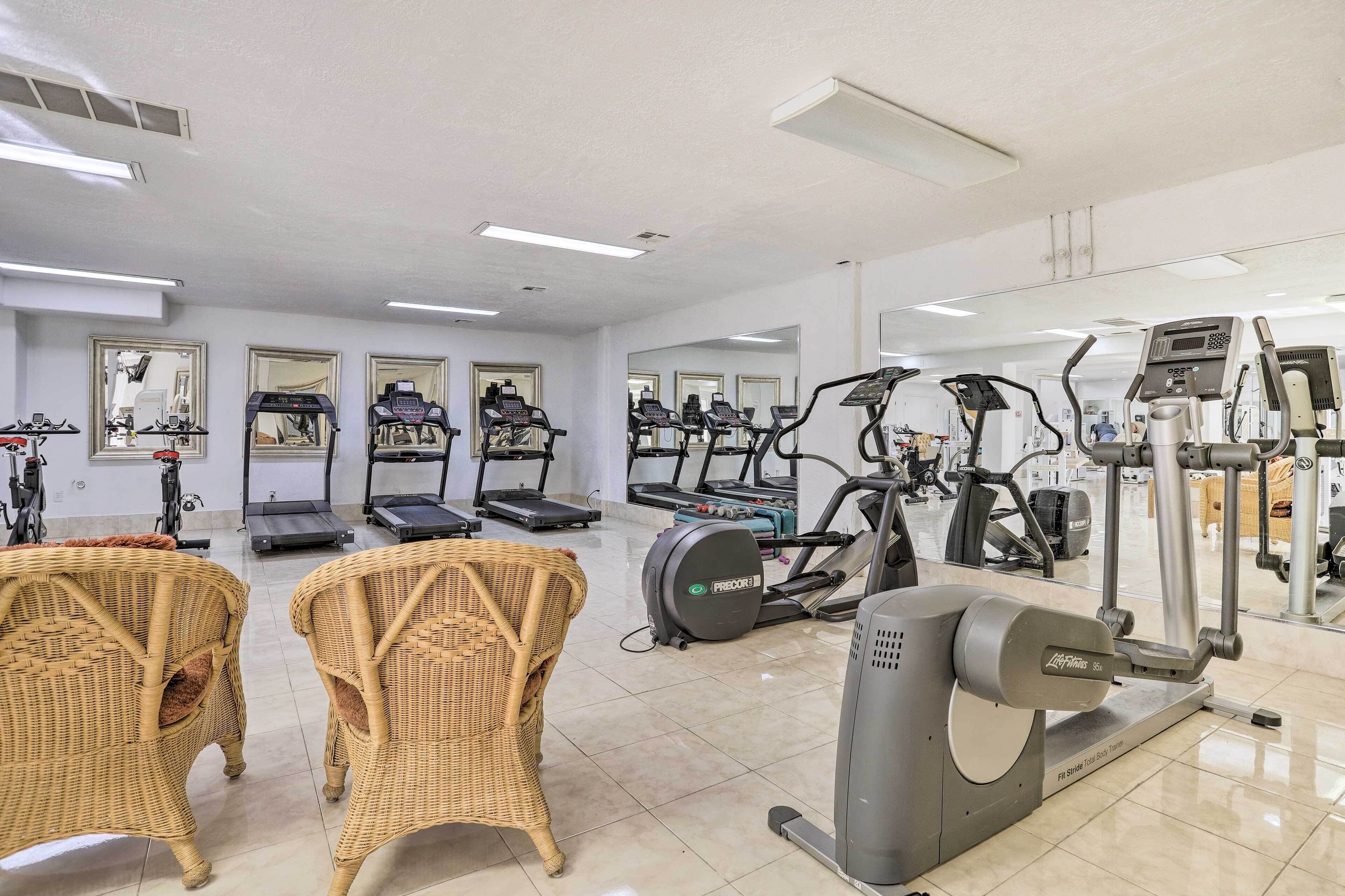 A gym with treadmills, ellipticals, and free weights. There are wicker chairs and a mirror on the wall.