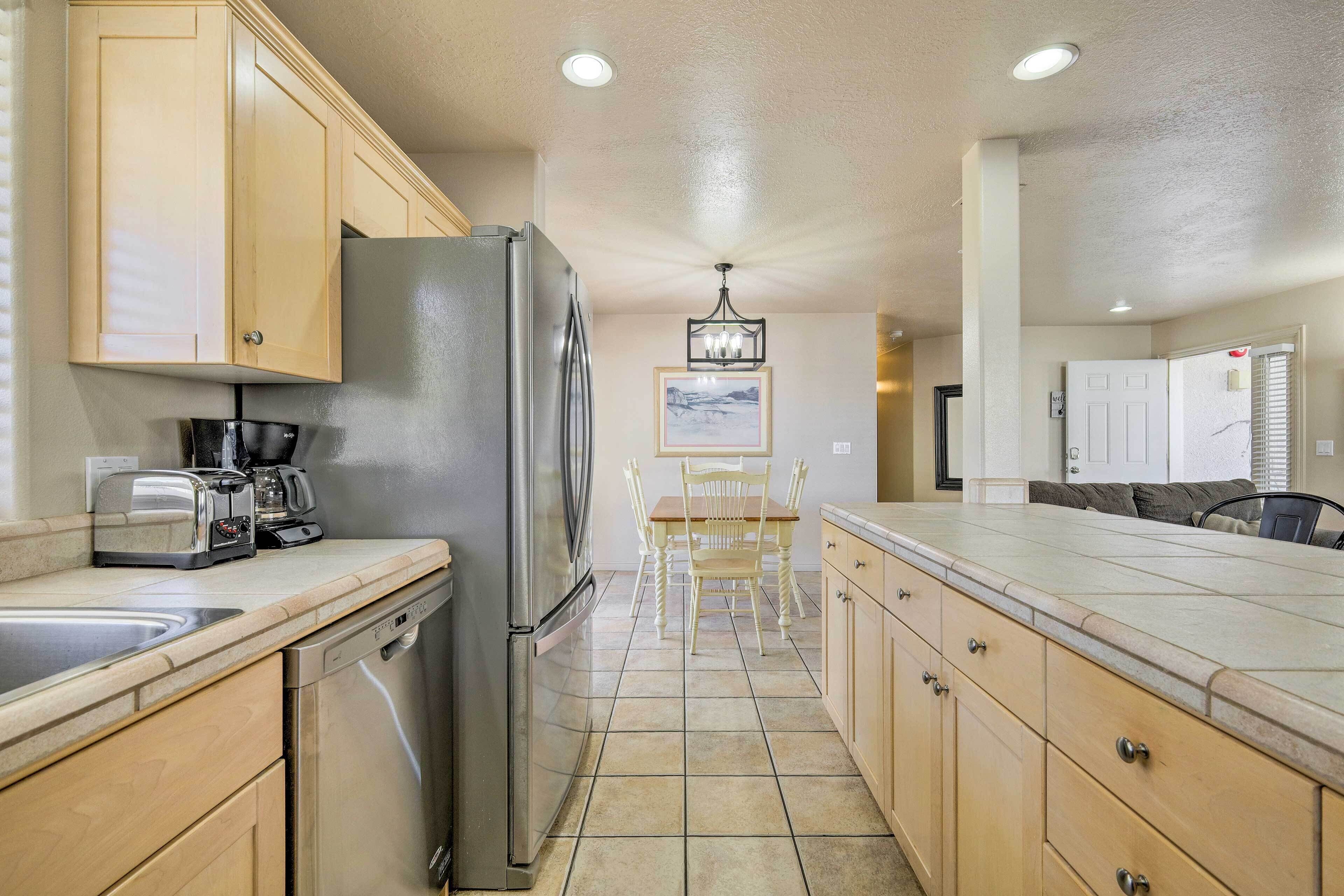 A kitchen with wooden cabinets, a stainless steel refrigerator, a dishwasher, a dining table with chairs, and a chandelier.