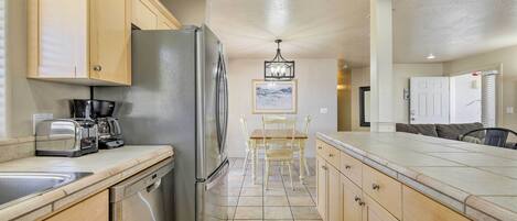 A kitchen with wooden cabinets, a stainless steel refrigerator, a dishwasher, a dining table with chairs, and a chandelier.