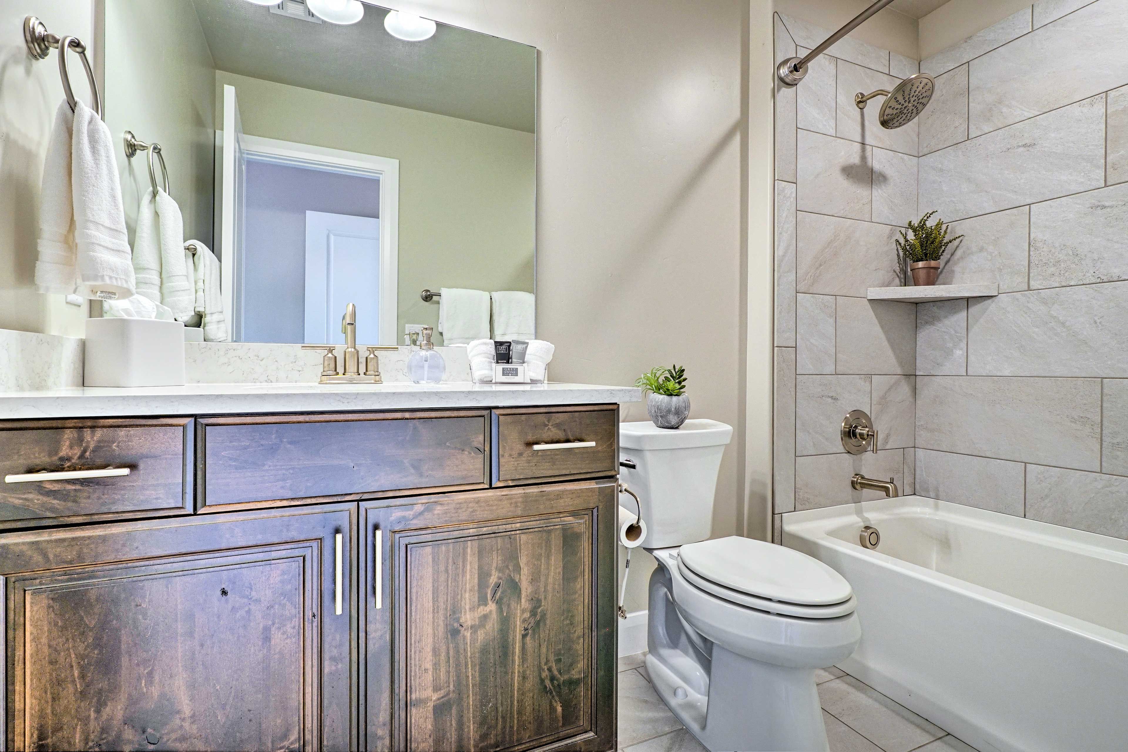 A bathroom with a wooden vanity, white toilet, and a bathtub with a showerhead.