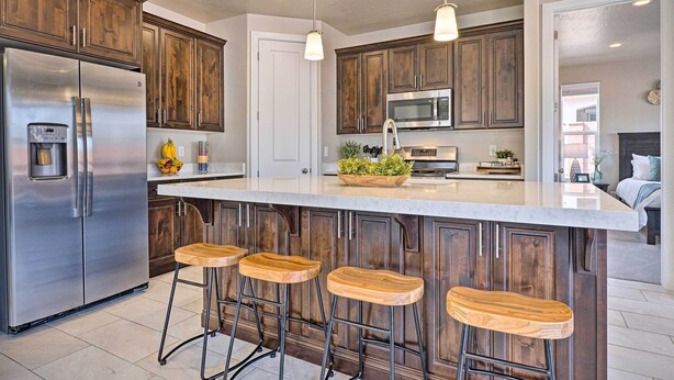 Eine moderne Küche mit Holzausstattung, Edelstahlgeräten, einer großen Kochinsel mit Barhocker, Pendelleuchten und Blick in den angrenzenden Wohnbereich.