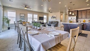 A spacious living area with a dining table set for six, a kitchen with dark wooden cabinets, and a ceiling fan. - Utah Group Getaway w/ Patio! Swim, Soak & Hike (Washington)