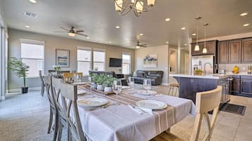 Un vaste espace de vie comprenant un coin repas avec une table pour six personnes, une cuisine dotée de meubles en bois foncé et un ventilateur de plafond.