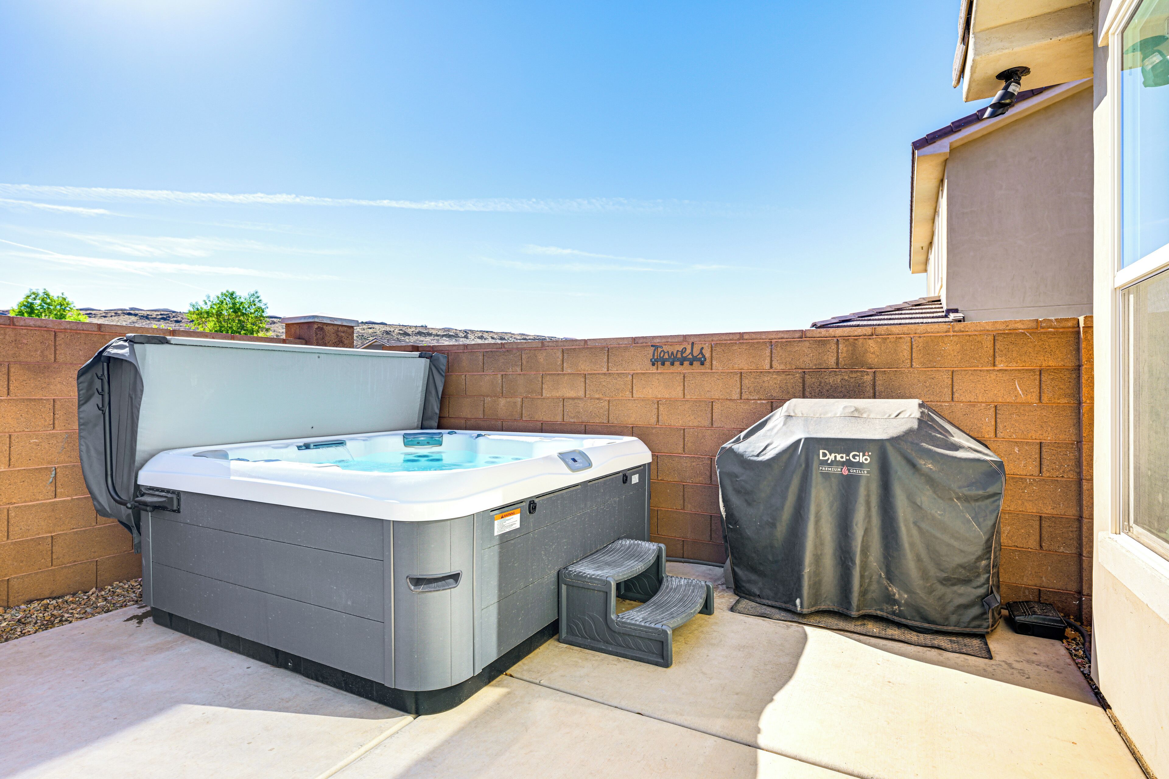 A hot tub with a cover, a step stool, and a grill cover in a backyard.