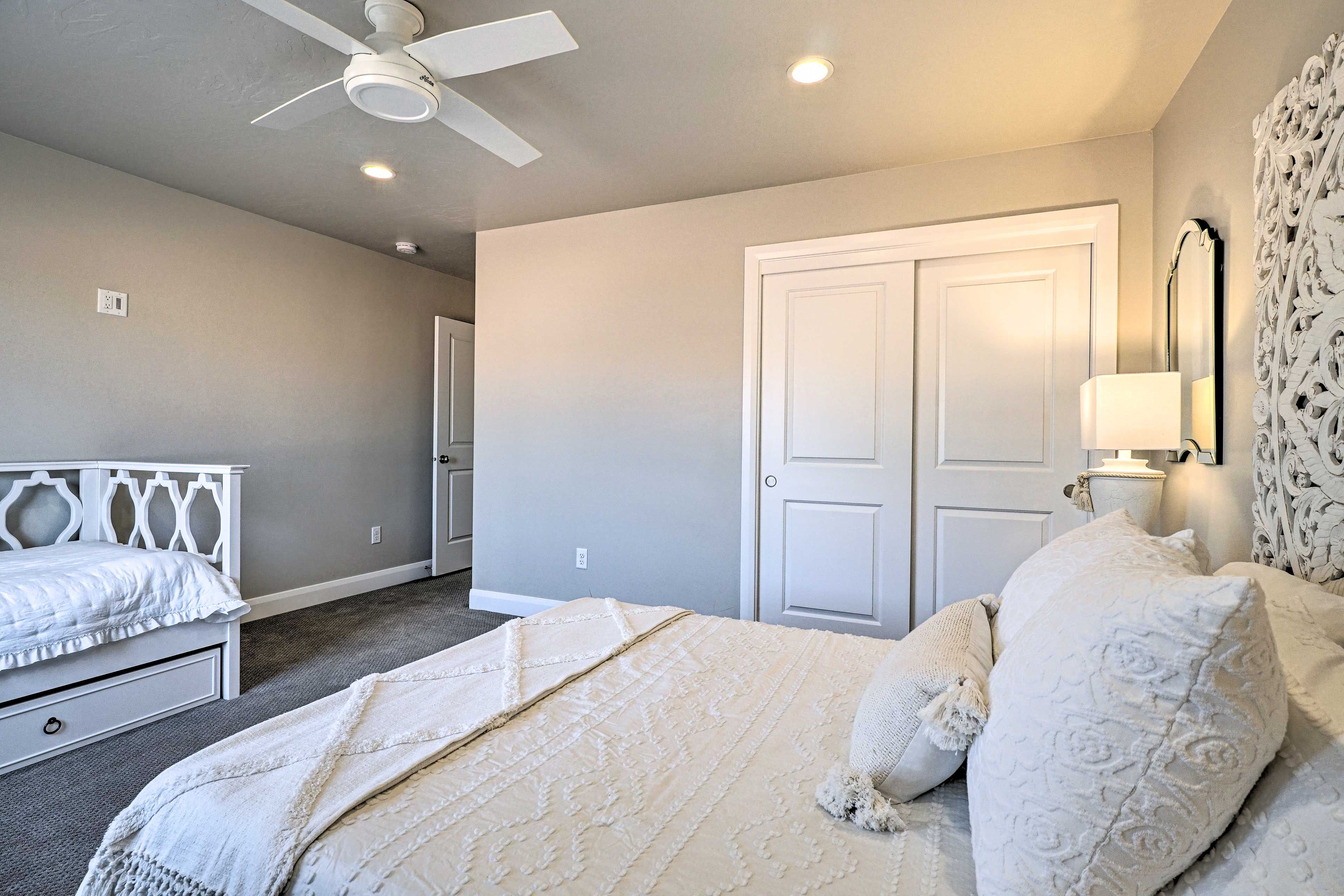 A bedroom with a bed, a ceiling fan, a door, and a wall-mounted lamp.