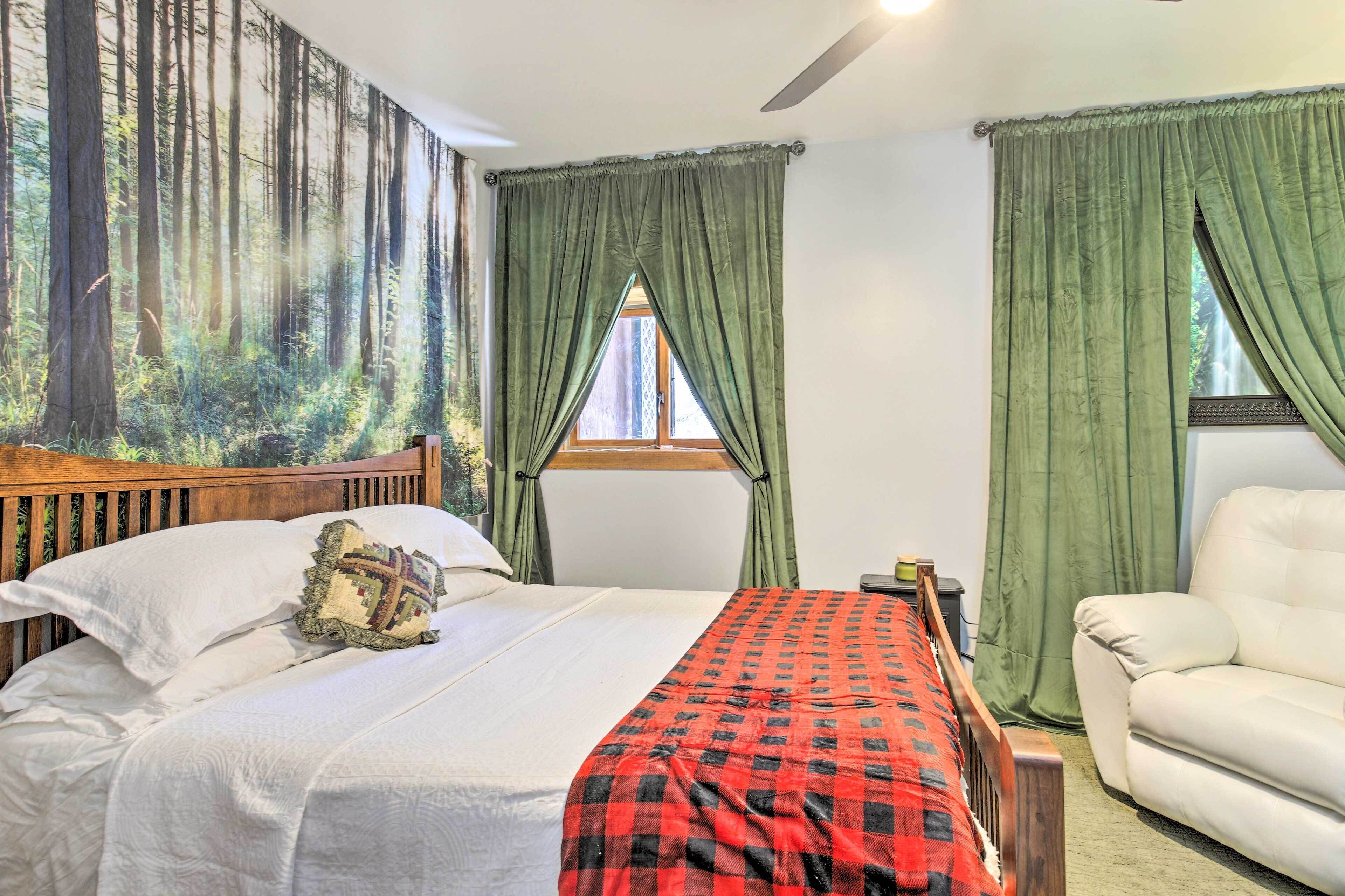 A bedroom with a bed, a chair, a window with curtains, and a wall with a forest mural.