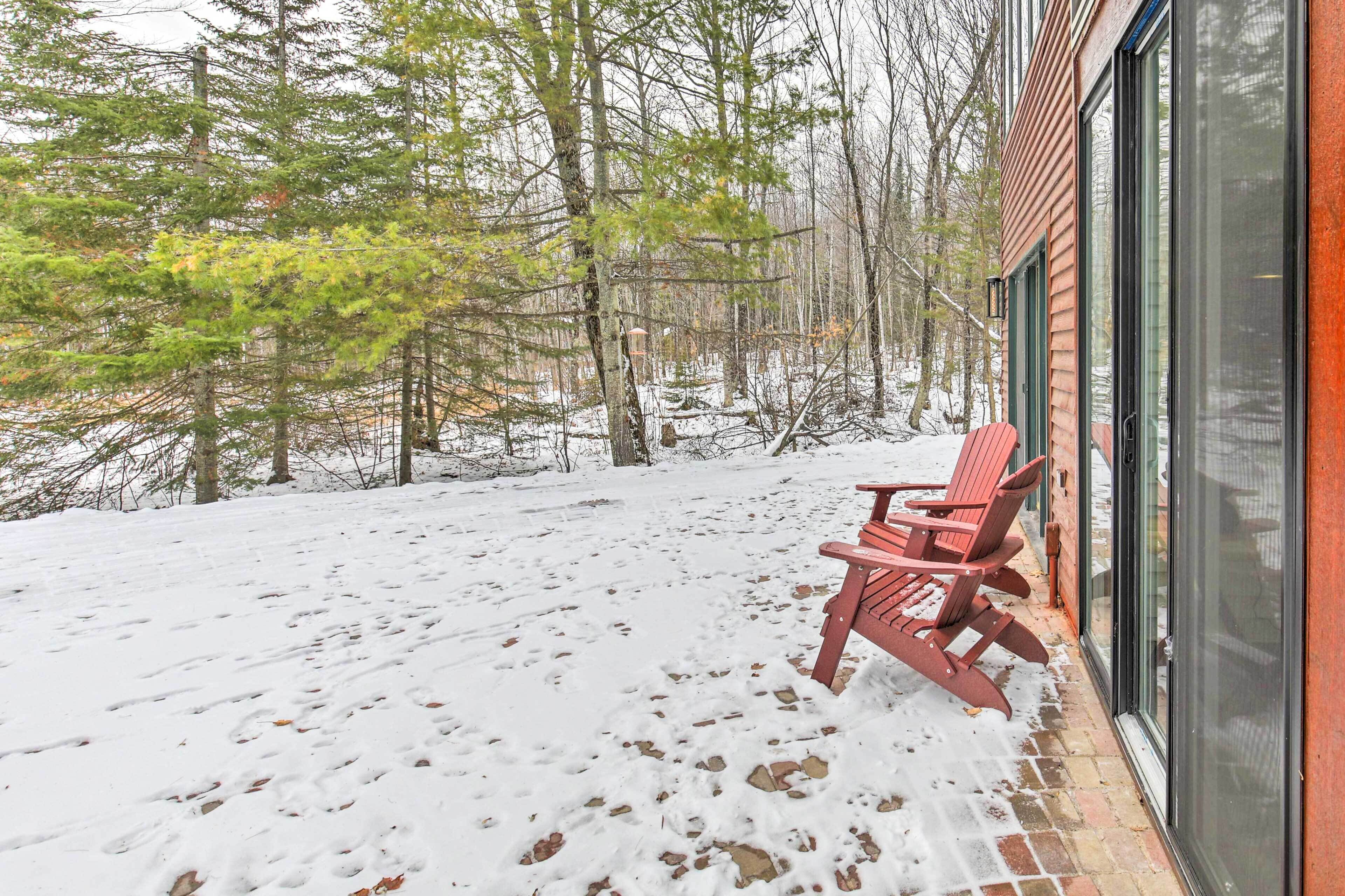 Une terrasse enneigée avec un banc en bois et une porte vitrée donnant accès à un bâtiment.