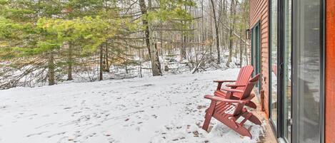 Une terrasse enneigée avec un banc en bois et une porte vitrée donnant accès à un bâtiment.
