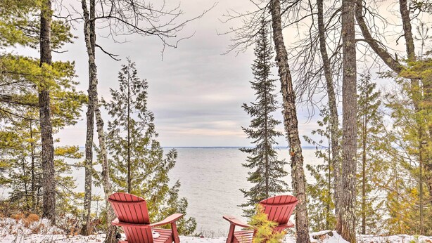 Dos sillas Adirondack rojas mirando hacia un lago con árboles al fondo.