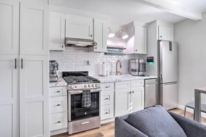 A modern kitchen with white cabinets, a built-in oven, a coffee machine, and a refrigerator.