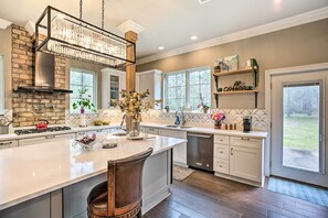 A modern kitchen with a large island, a built-in stove, and a hanging light fixture.