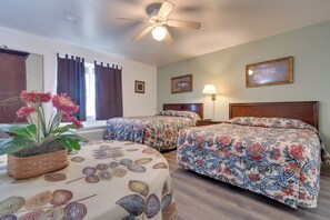 Habitación de hotel con dos camas, ventilador de techo, planta en maceta y ventana con cortinas.