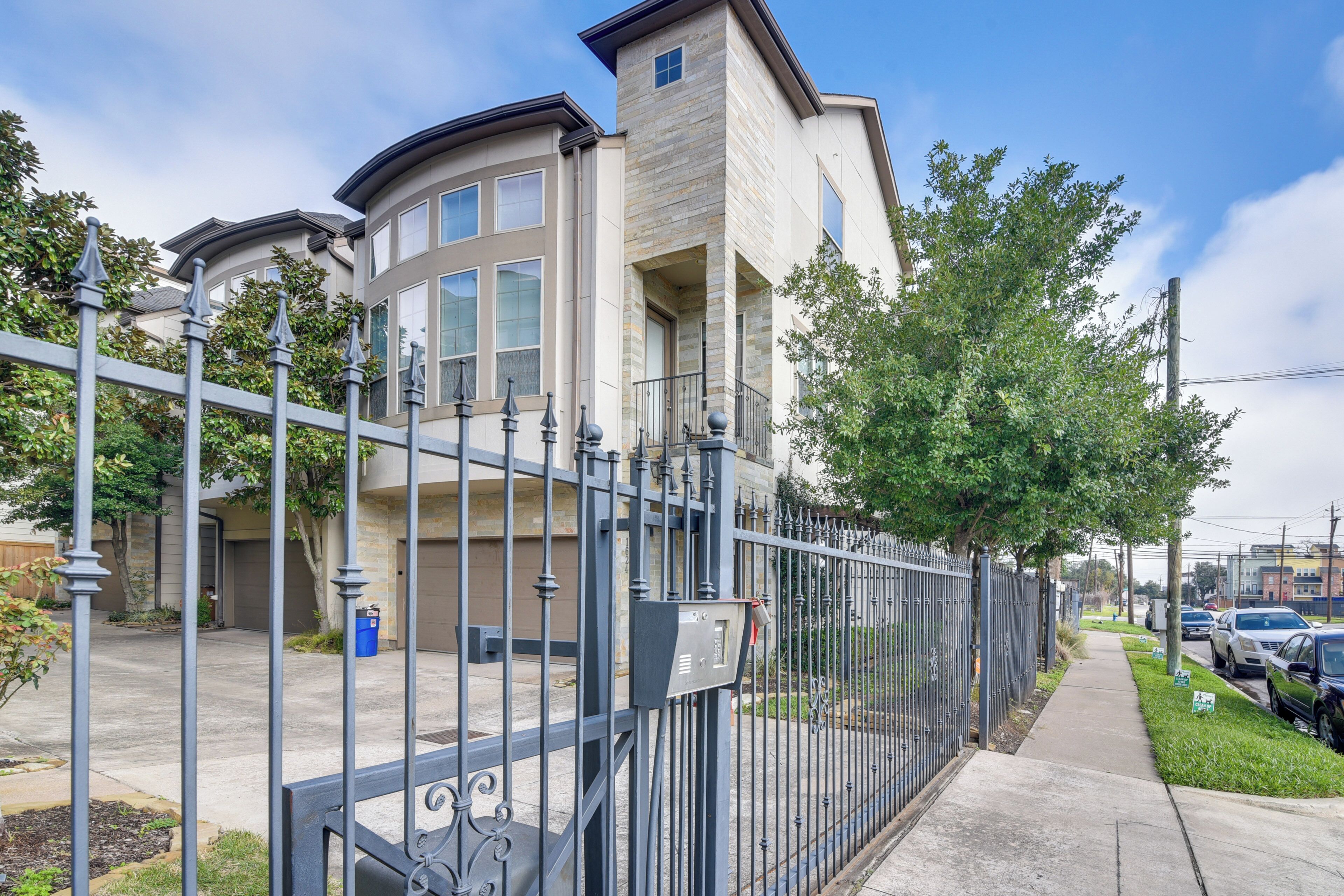 A gated residential area with a modern house featuring a stone facade, large windows, and a garage.