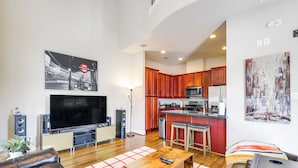 A modern living room with a flat-screen TV, leather sofas, a coffee table, and a kitchen in the background.
